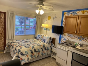 small studio, queen bed, colorful blue/white comforter, white kitchen, beige tile floor